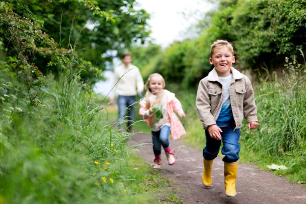 brother and sister running along woodland path 