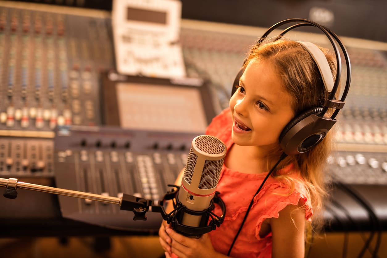 Happy little girl enjoying while talking over a microphone during radio broadcast.