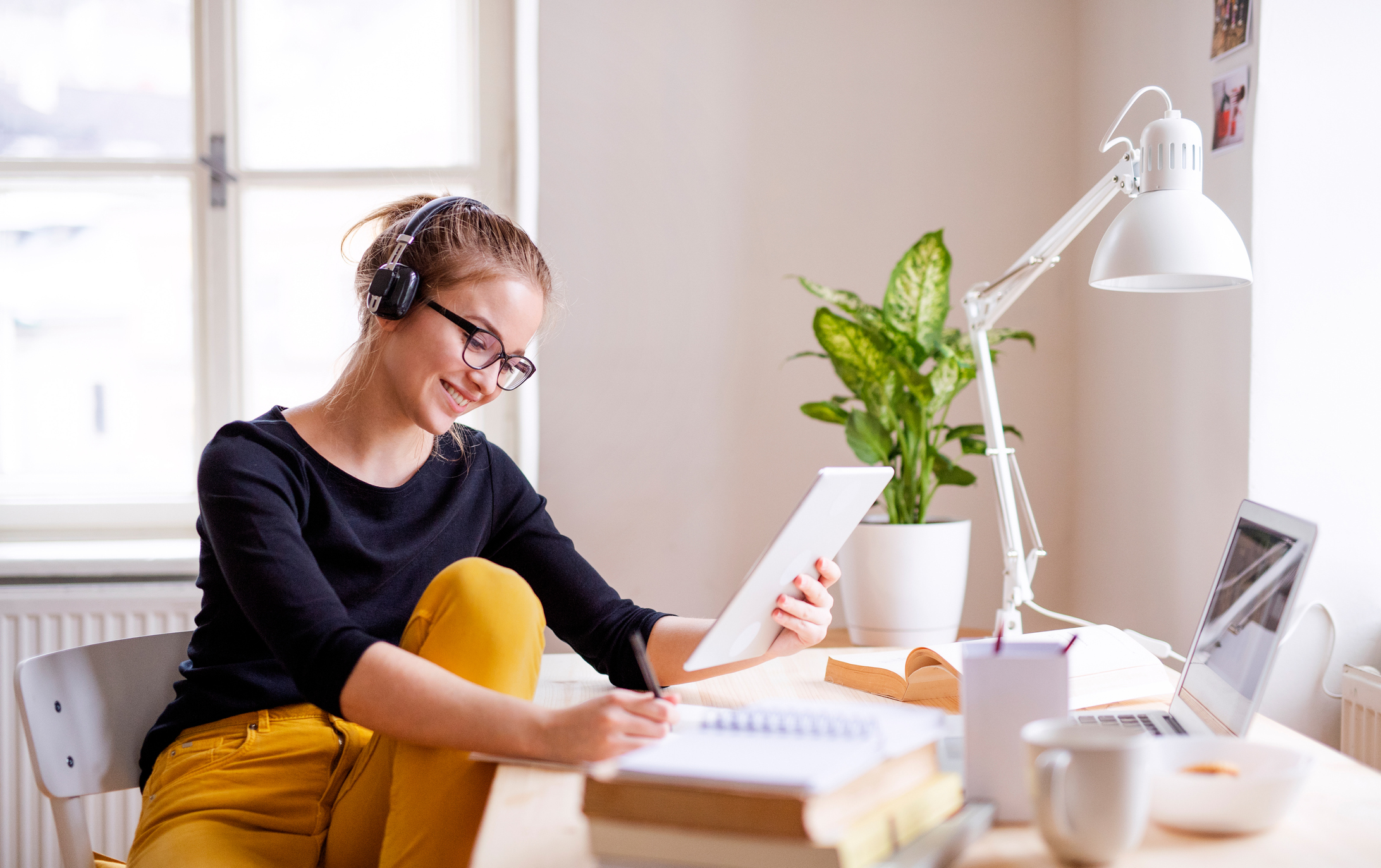 A young female student sitting at the table, using a tablet while studying.