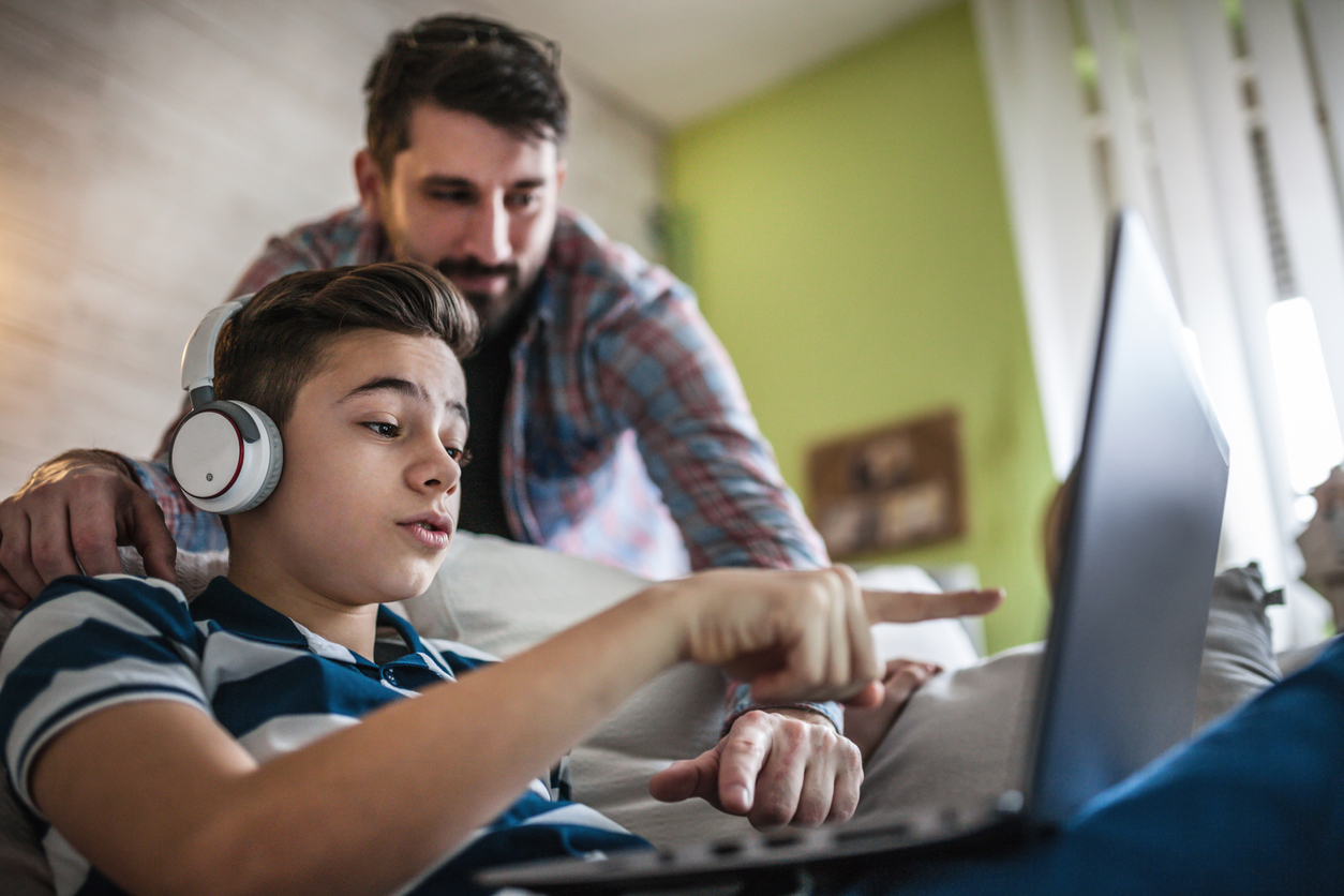 Smiling foster father and son using digital gadgets in living room