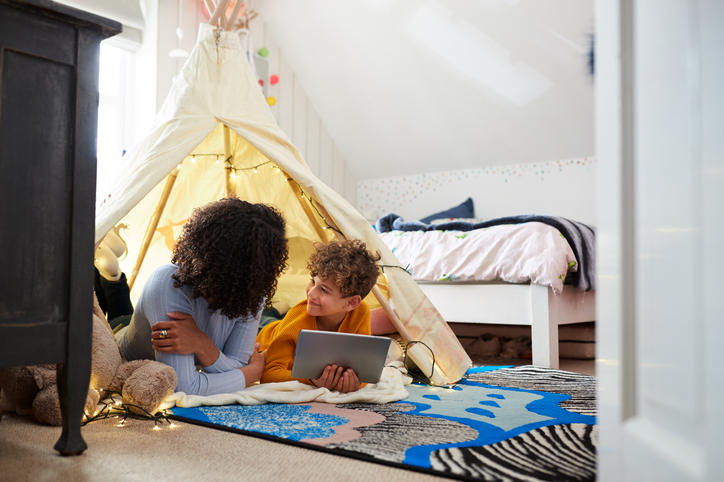 Foster carer with young boy reading in a bedroom fort