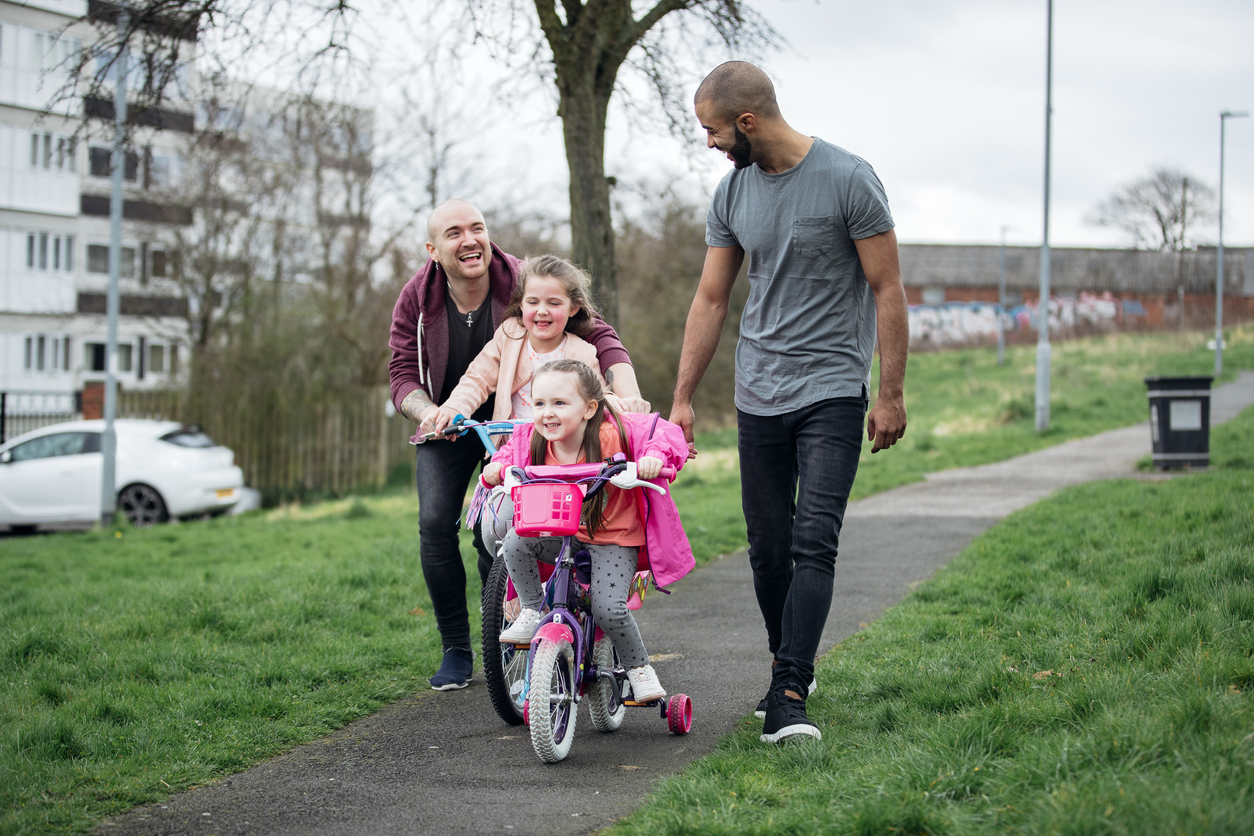 Young male couple taking their daughters out riding their bicycles in the housing estate