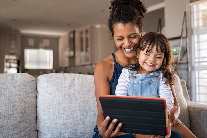 Carer and child using digital tablet on couch.