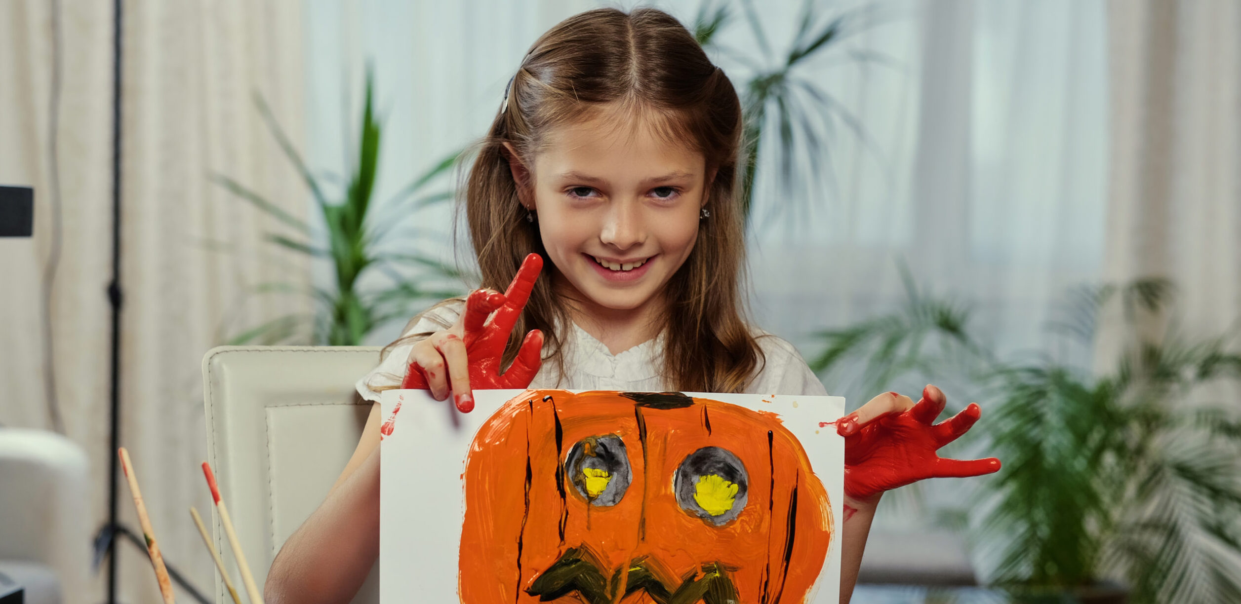 A girl holds a poster with painted Halloween pumpkin.