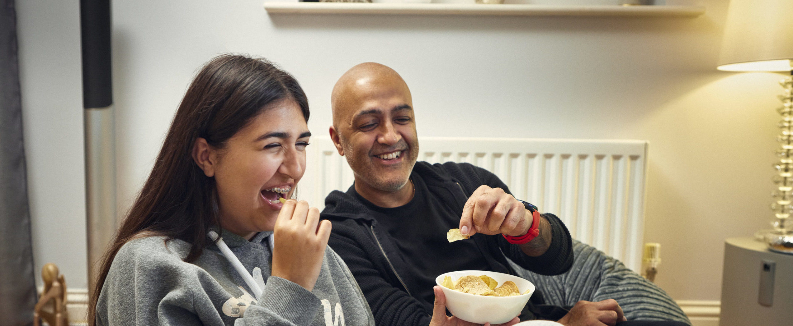 Foster carer and foster child, laughing and eating crisps.